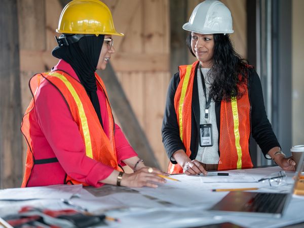 Two female architects reviewing blueprints at a construction site.