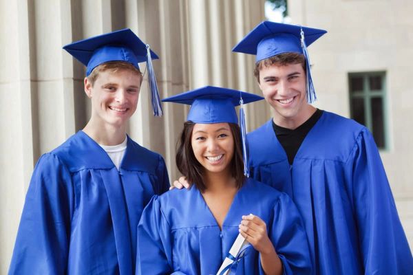 Three graduates in blue caps and gowns smiling joyfully.