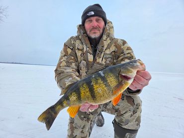 Man in camouflage holding a large fish on a snowy landscape.