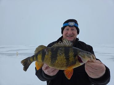 Man holding a large fish on a snowy, icy lake.