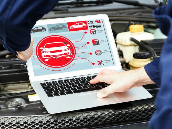 Laptop mechanic next to car engine. Modern on-screen diagnostic software.