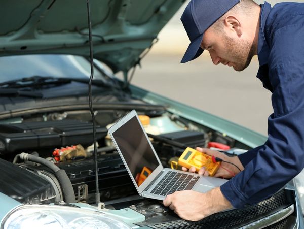 Mechanic using computer diagnostics while repairing car
