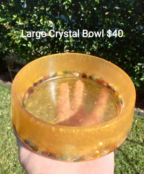 Hand holding a large golden crystal bowl with colorful stones inside.