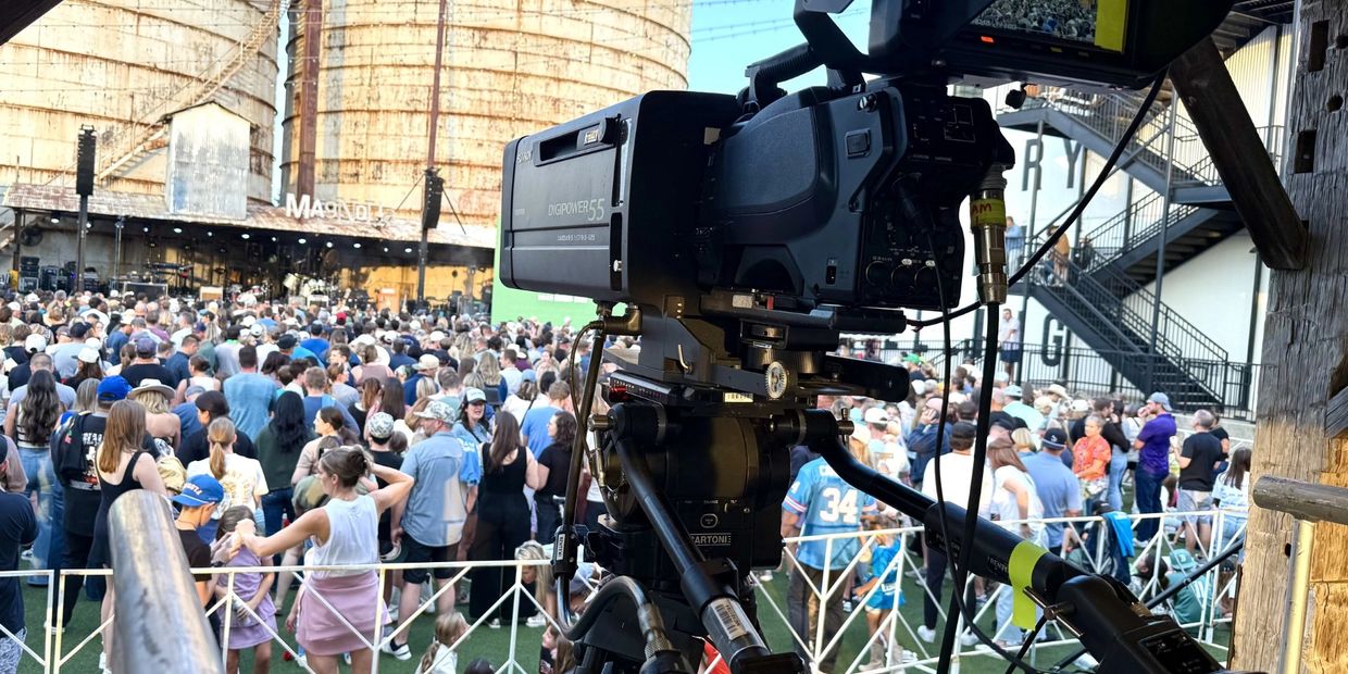 Professional camera filming a crowded outdoor event at Magnolia venue.