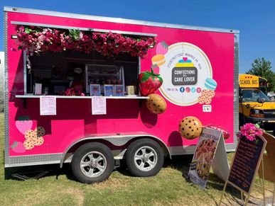 Bright pink food truck selling cookies and desserts at an outdoor event.
