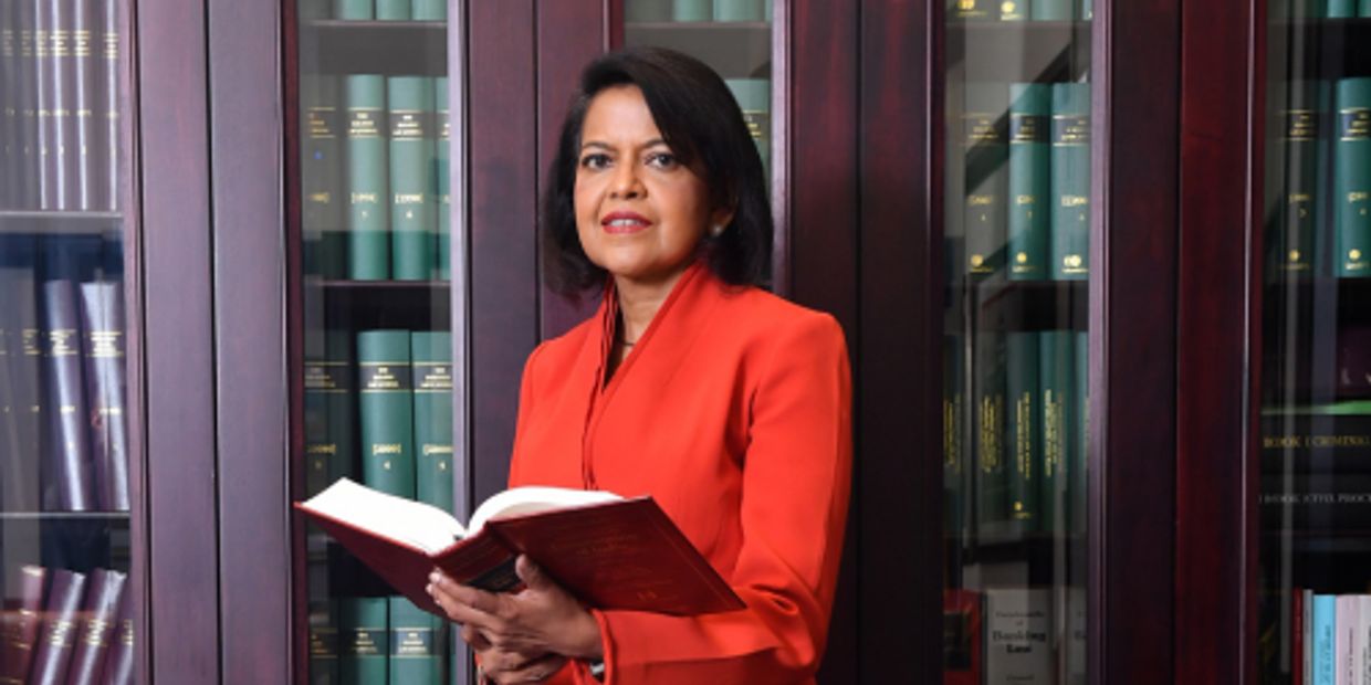 Woman in orange holding a book in front of a bookshelf.