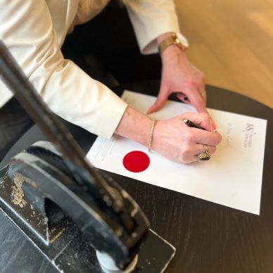 Person signing an official document with a red seal.