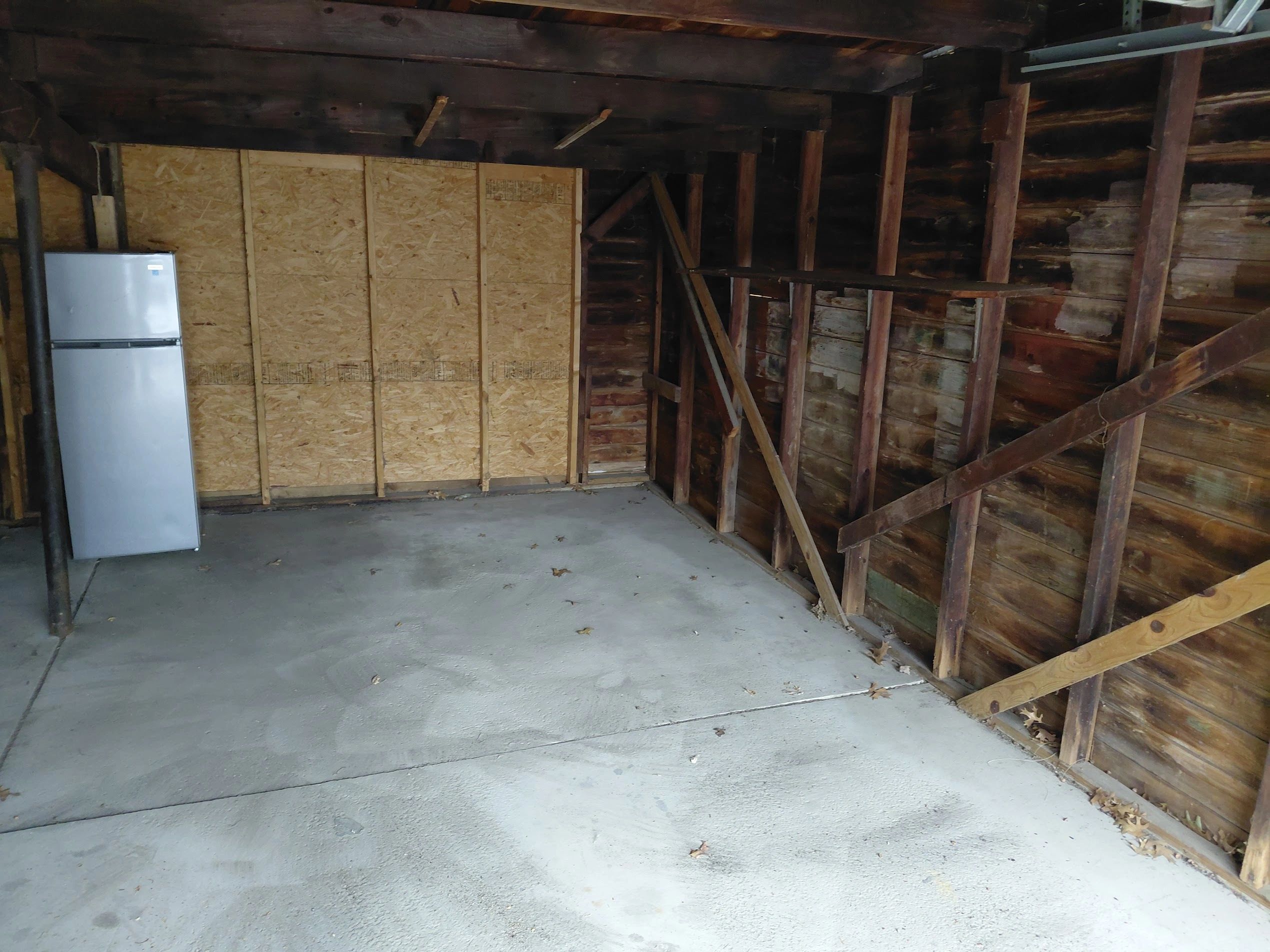 Empty garage with wooden walls and a refrigerator.
