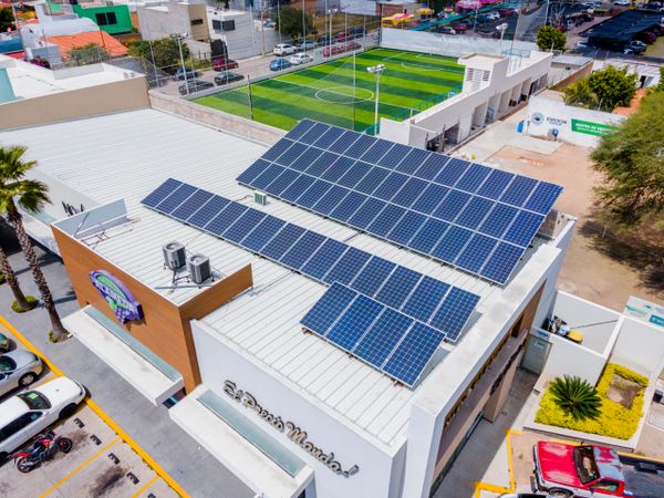 Building rooftop covered with solar panels and a nearby sports field.