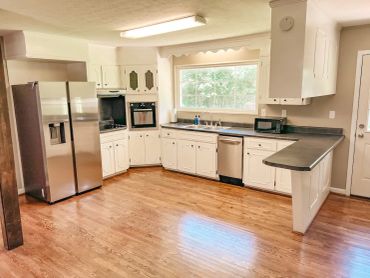 Spacious kitchen with wooden floors and white cabinets.