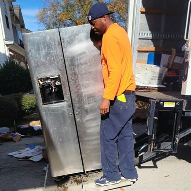 Junk remover in Atlanta removing stainless steel refrigerator from garage and placing it onto truck