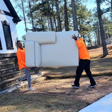 Two men moving portion of sectional sofa out to truck for junk removal in Lithia Springs, GA