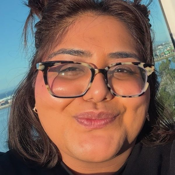 Person smiling outdoors with tortoiseshell glasses and sunlight on face.