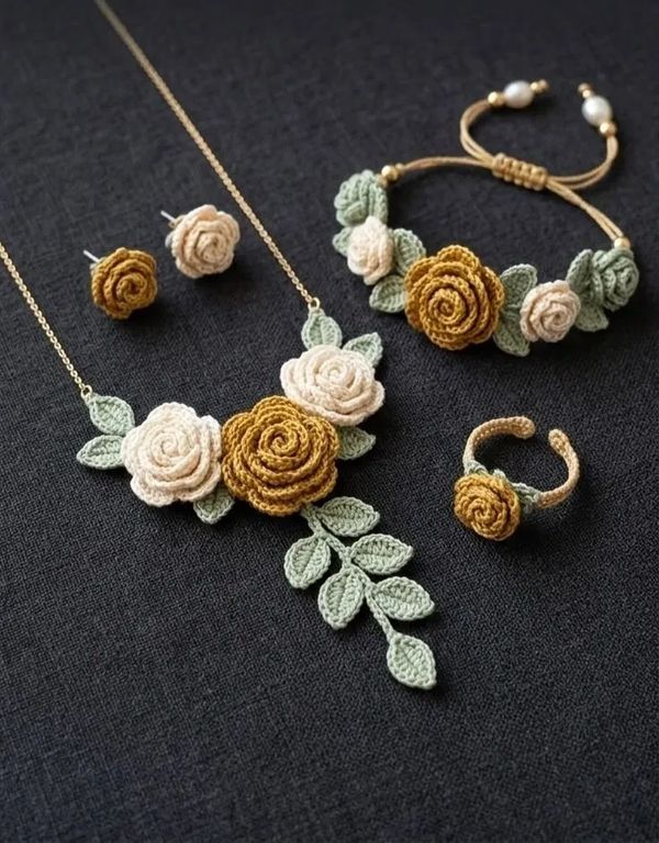 Crocheted floral jewelry set with necklace, bracelet, ring, and earrings on black fabric.