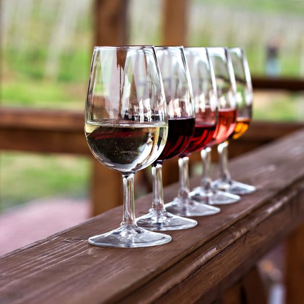 Five wine glasses with different colored wines lined up on a wooden railing.