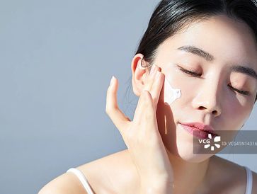 Woman applying cream on her face with eyes closed.