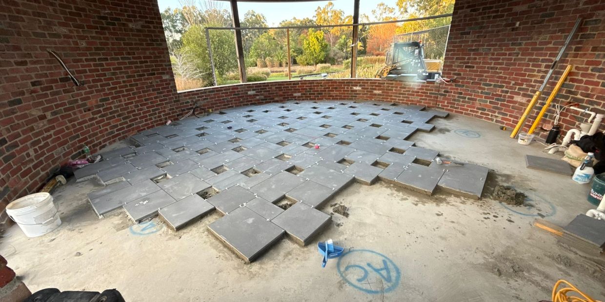 Floor tiling in progress on a curved brick wall patio with outdoor view.