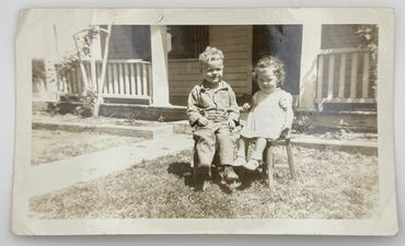Two children are sitting in the front yard.