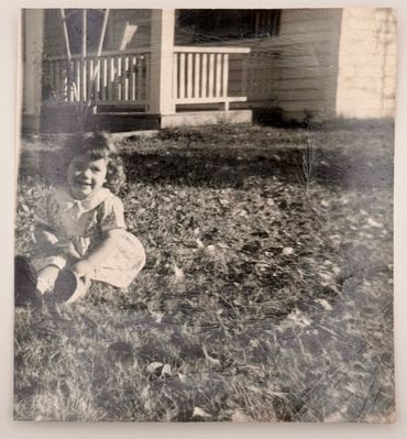 A little girl sitting in the front yard.