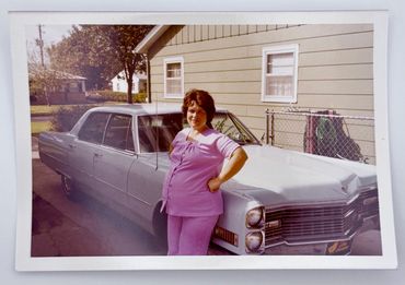 A woman leaning against a car in a driveway.