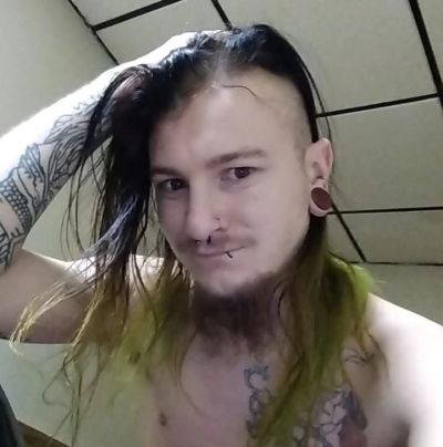 Person with tattoos, piercings, and half-shaved hair.