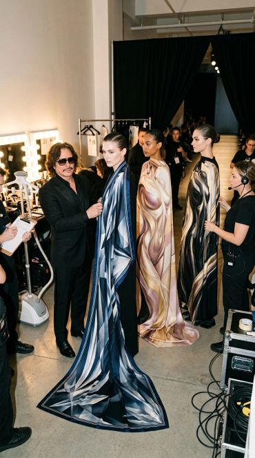 Models draped in artistic fabrics backstage at a fashion event.