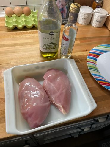 Chicken breasts on a kitchen counter with olive oil and white wine vinegar.