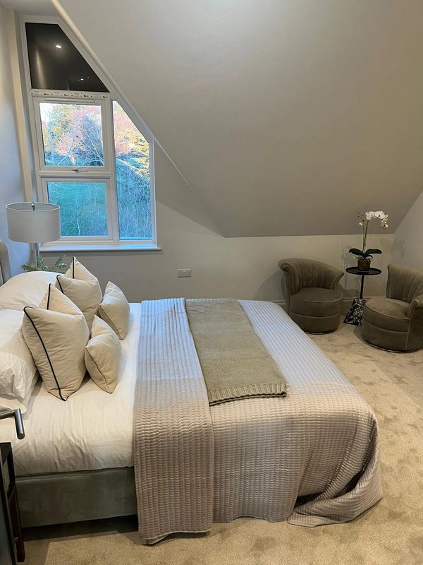 Cozy bedroom with neutral tones and an angled window revealing a scenic view.