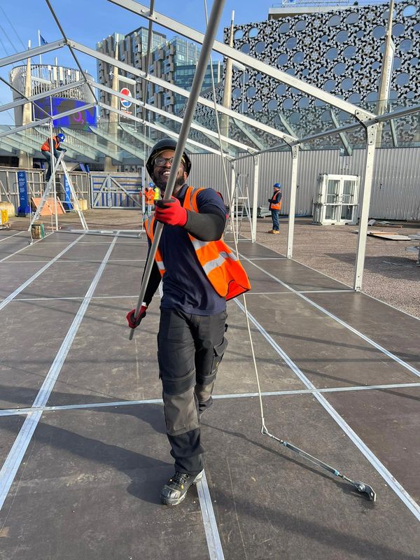 Construction worker assembling a metal framework outdoors under clear skies.