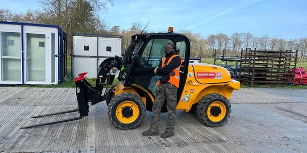 Worker posing with a yellow forklift on a concrete surface outside.