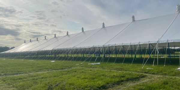 Large white event tent set up on green grass under a cloudy sky.