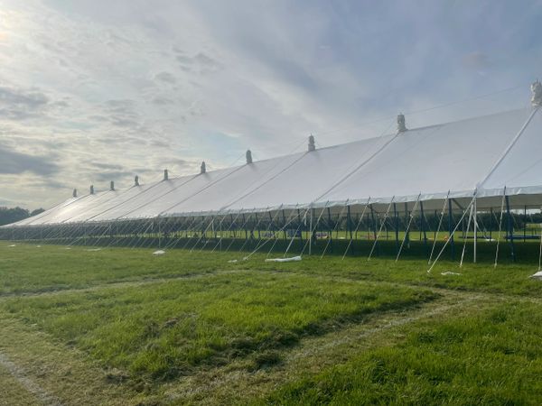 Large white event tent set up on green grass under a cloudy sky.