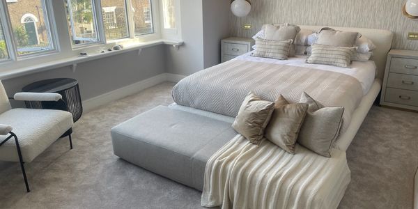 Modern bedroom with beige tones and natural light from large windows.