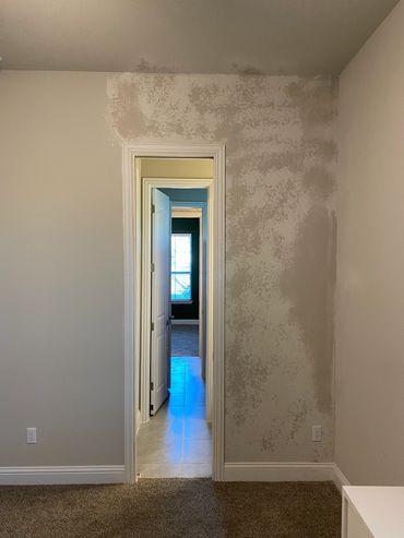 Wall with patchy paint near a doorway leading to a bright room.