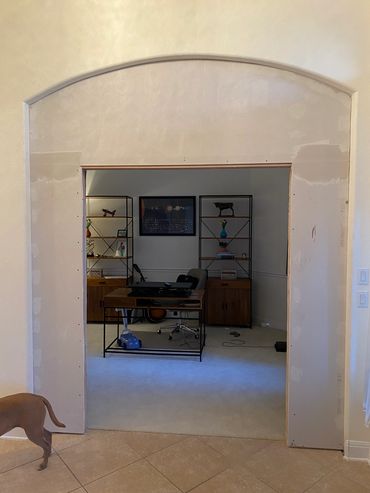 Partially renovated office room with a desk, shelves, and a dog walking away.