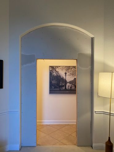 Unfinished arched doorway with exposed drywall and a black-and-white photo inside.