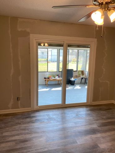 Room with sliding glass doors leading to a sunlit patio and unfinished drywall.
