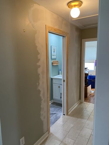 Hallway with unfinished wall painting and open doors leading to bathroom and another room.