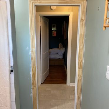 Doorway with unfinished wooden trim and mixed flooring in a home interior.
