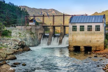 A dam with water flowing over it in a mountainous area.