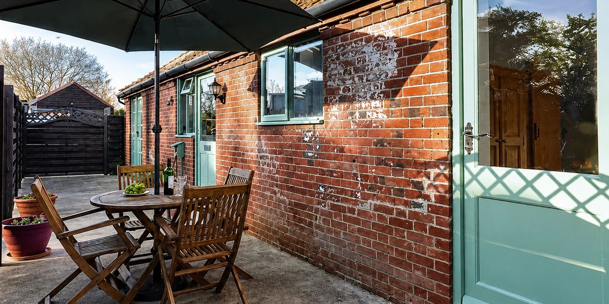 Cozy outdoor patio with wooden furniture and a large umbrella beside a brick house.