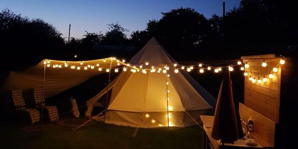 Cozy nighttime camping setup with a lit tent and string lights.