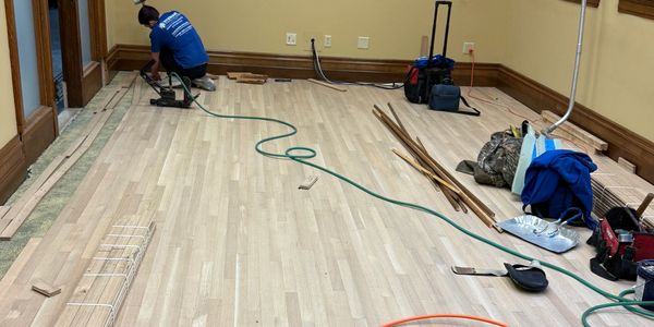 Worker installing light-colored wooden flooring in a room.