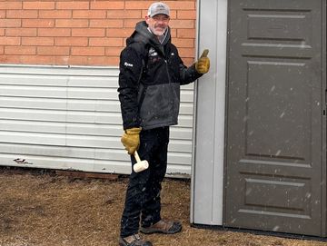 Man in winter gear standing next to a shed door giving a thumbs up.