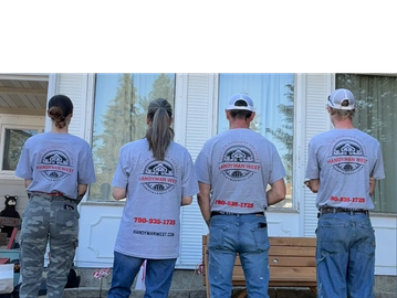 Four people wearing matching HandyMan West t-shirts stand with their backs to the camera.