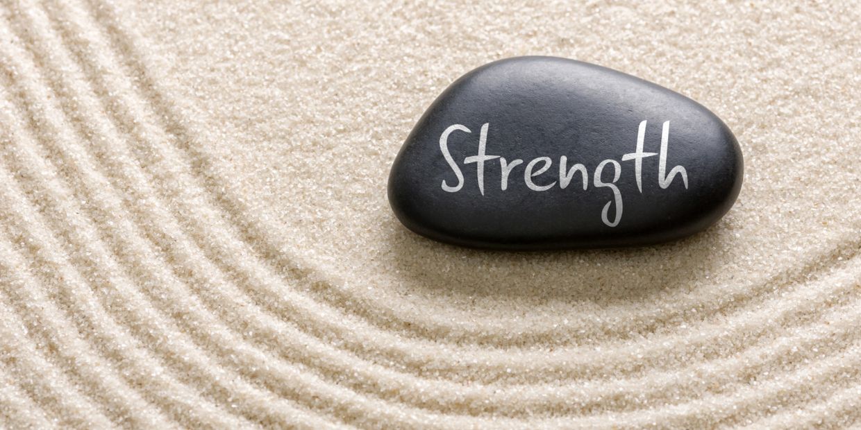 A black stone inscribed with "Strength" on raked sand.