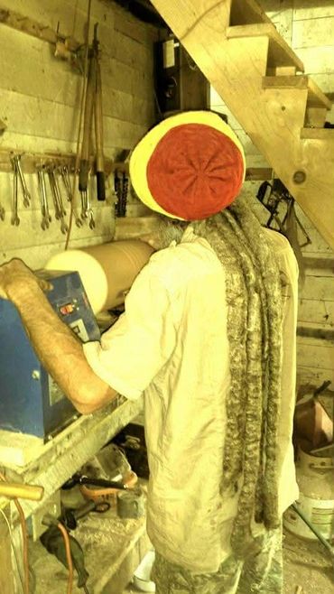 Man with long dreadlocks working on a lathe in a workshop.