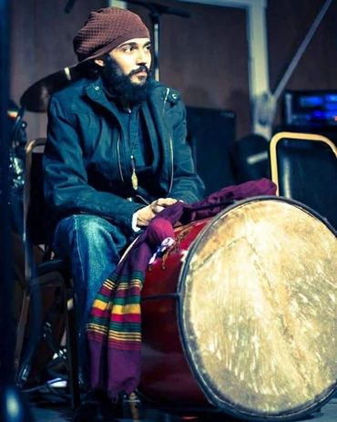 Man in beanie sitting with a large drum and colorful cloth.