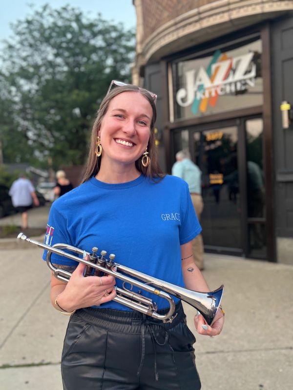 Smiling woman holding trumpet outside Jazz Kitchen.
