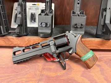 Black revolver with wooden grip displayed on a wooden surface.